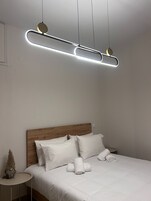 Un dormitorio moderno con cabecera de madera, ropa de cama blanca y una lámpara de techo original.
