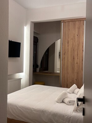 Un dormitorio con cama, armario de madera, taburete pequeño y televisor montado.