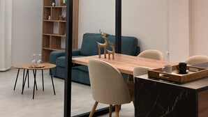 A modern living room with a wooden dining table, chairs, a sofa, and a bookshelf. - Abete Luxury Apartments (Metsovo)