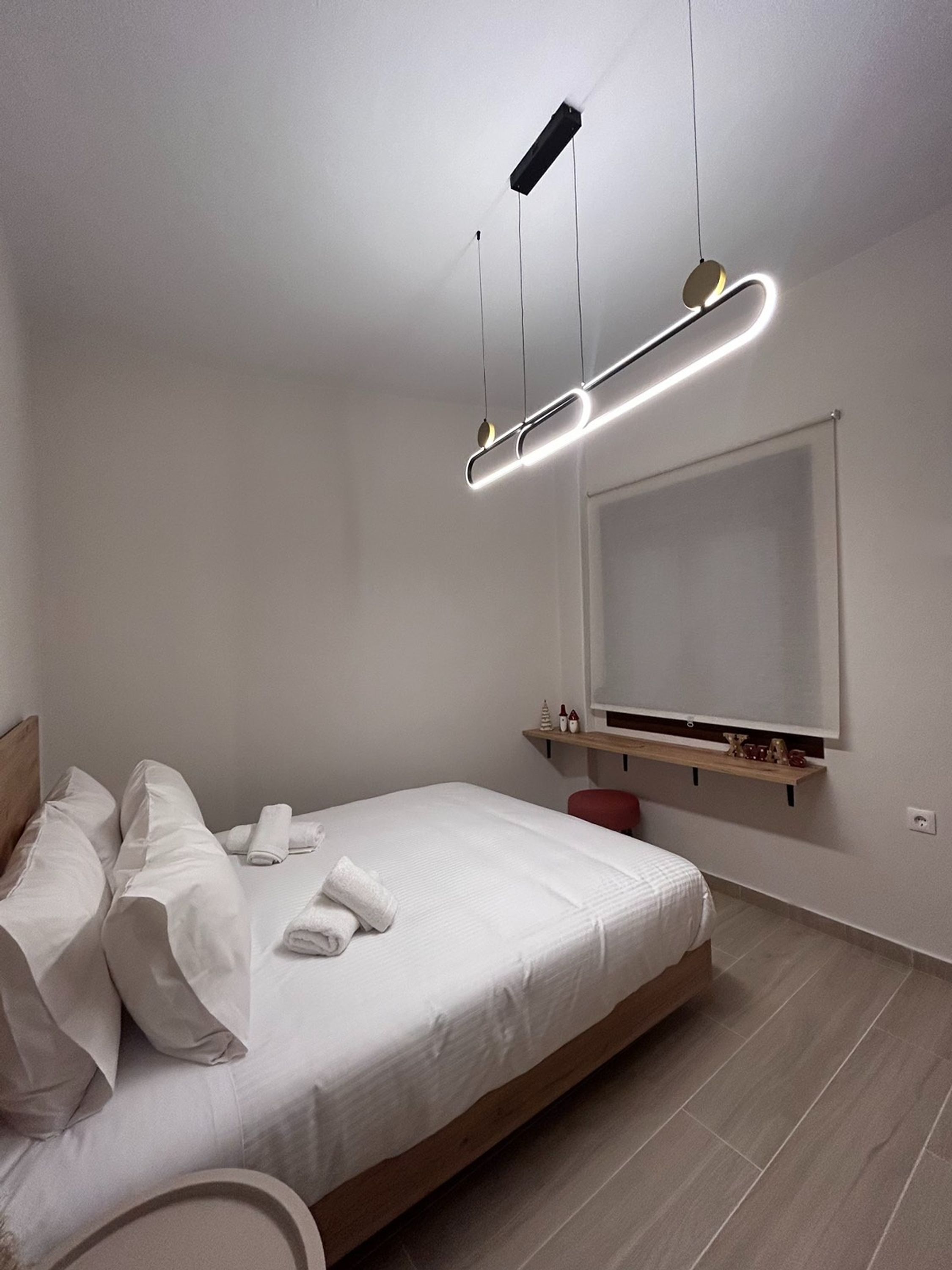 A modern bedroom with a bed, a bedside table, a TV mounted on the wall, and a ceiling light fixture.