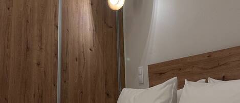 Quarto com guarda-roupa de madeira, cama com roupa de cama branca e luminária pendente.