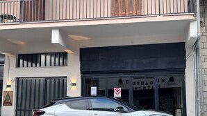 A white SUV parked in front of a building with a 'No Parking' sign, a gated entrance, and a balcony with a railing. - Abete Luxury Apartments (Metsovo)