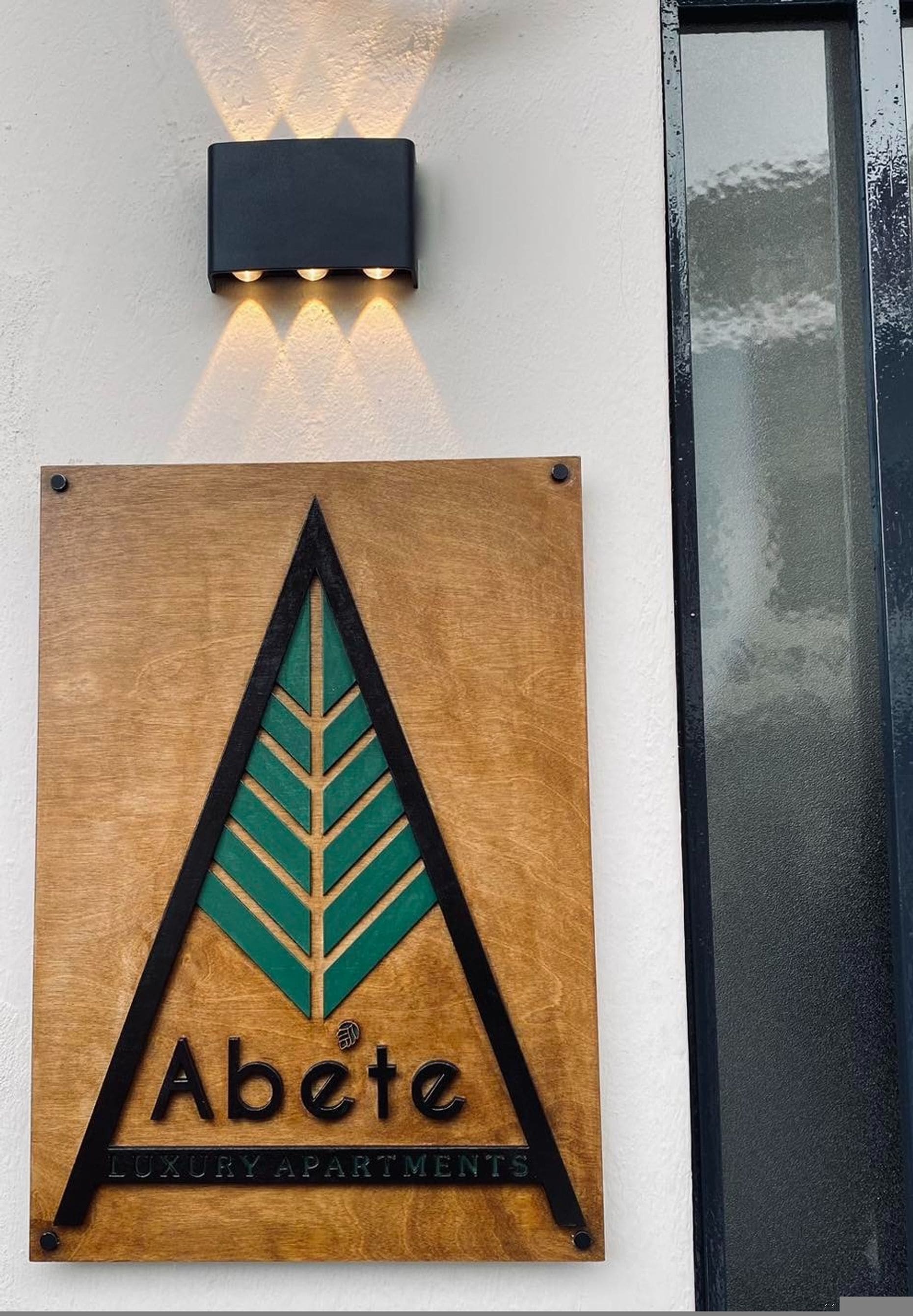 A wooden sign with a leaf design and the text "Abete Luxury Apartments" mounted on a wall.