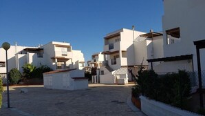 Zona residencial con edificios blancos, un patio empedrado y cielo azul despejado.