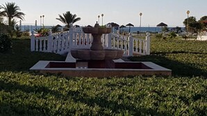 Una fuente en un área ajardinada con una valla blanca y palmeras.