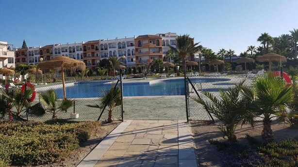 Un hotel con piscina, palmeras y un cielo azul despejado.