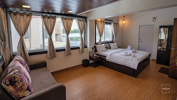 A hotel room with a bed, a bedside table, a chair, and a window with curtains. - Have fun with the whole family at this Stylish 4 Bedroom private pool Villa (Lonavala)