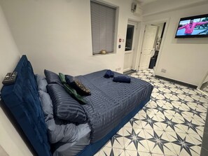 Ein Schlafzimmer mit Bett, Kissen, einer Fernbedienung und einem Fernseher an der Wand.