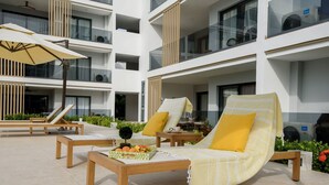 A modern outdoor lounge area with wooden furniture, yellow cushions, and a fruit basket on a table. - Bran new condo with pool access (Bavaro)