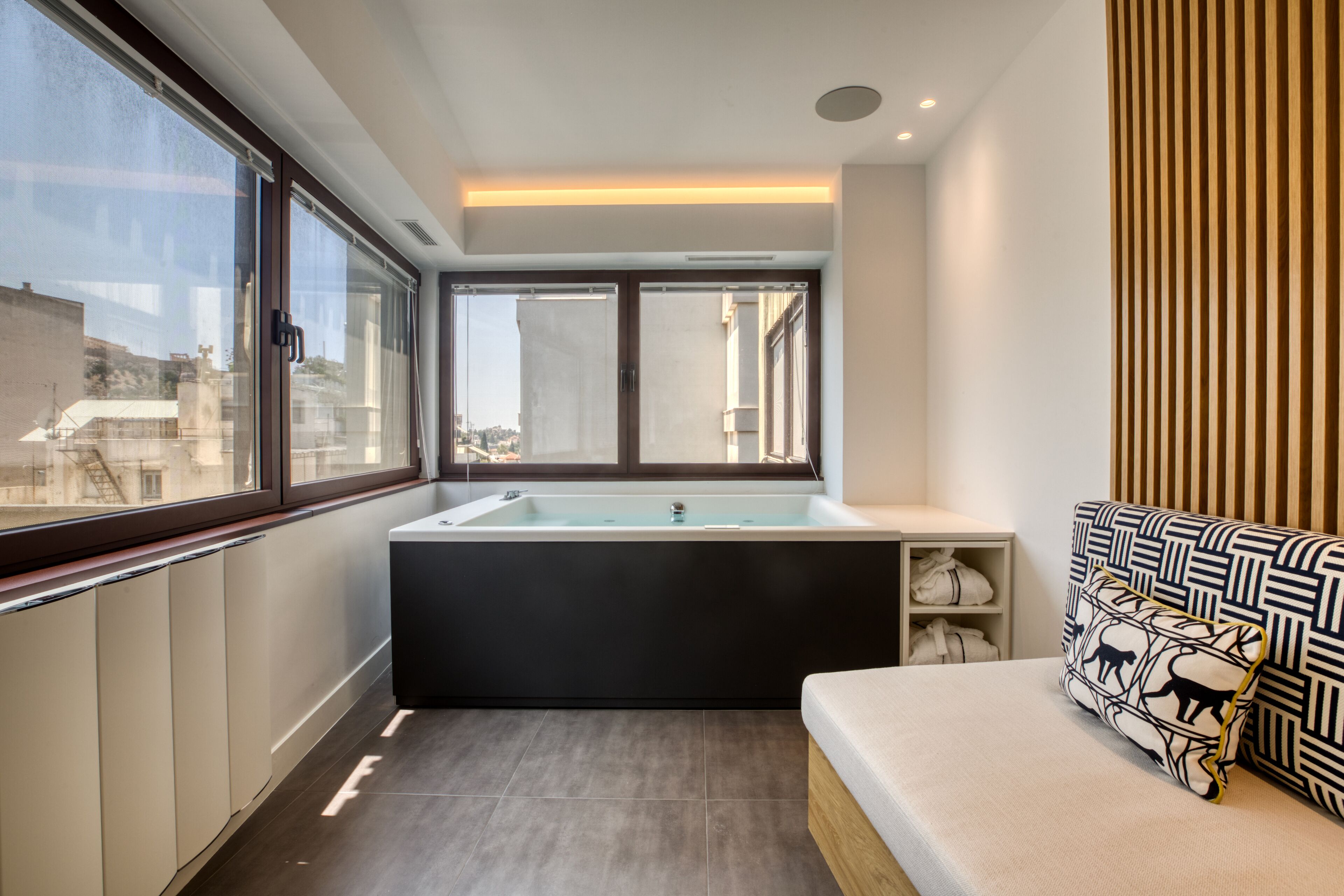 A modern bathroom with a bathtub, a window, and a sofa with patterned cushions.