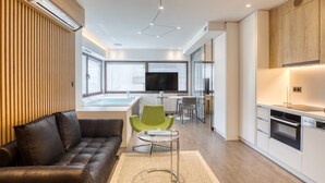 A modern kitchen with a built-in oven, a dining area with a green chair, and a living area with a leather sofa. - GSM Elevated Luxury Suites (Athens)