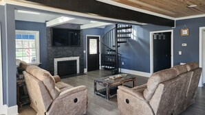 A spacious living room with a fireplace, two recliner sofas, a coffee table, and a spiral staircase. - The Salty Dog (Conway)