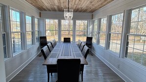 A spacious sunroom with a large wooden table and chairs, large windows, and a wooden ceiling. - The Salty Dog (Conway)