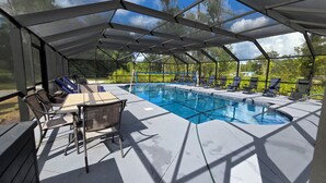 A covered outdoor swimming pool with lounge chairs and a table. - The Salty Dog (Conway)