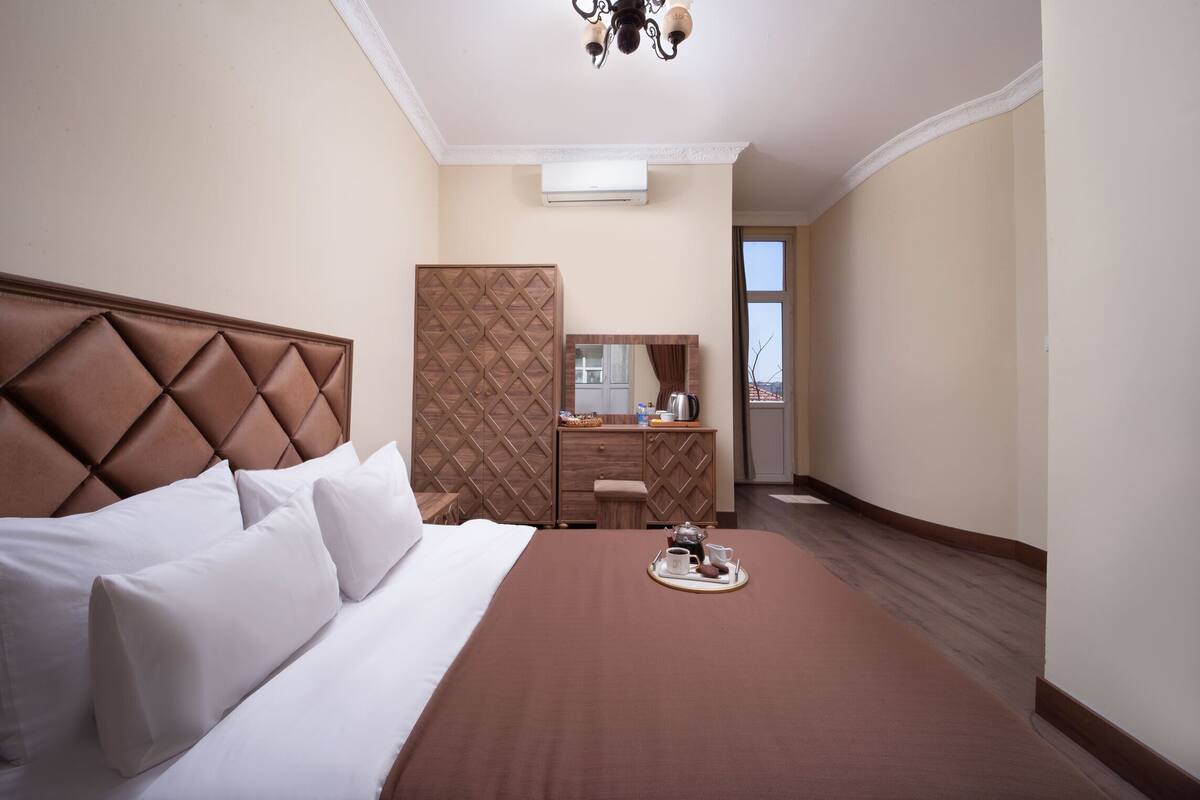 A hotel room with a large bed, a dresser, a mirror, and a breakfast tray on the bed.
