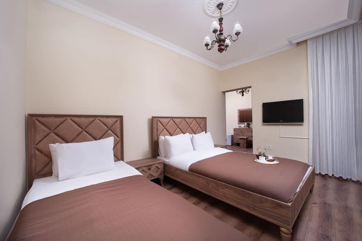 A hotel room with two beds, a TV, a mirror, and a chandelier.