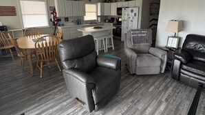 A modern living room with a leather armchair, a grey sofa, and a dining area with wooden chairs and a table. - Beach Cottage, 3 min walk to Beach Kill Devil Hills with WiFi, AC, Hot Tub (Kill Devil Hills)