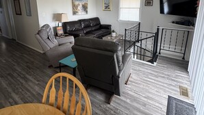 A living room with a sectional sofa, a TV, and a staircase leading to an upper level. - Beach Cottage, 3 min walk to Beach Kill Devil Hills with WiFi, AC, Hot Tub (Kill Devil Hills)