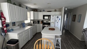 A modern kitchen with white cabinets, a central island, and a dining table with a placemat. - Beach Cottage, 3 min walk to Beach Kill Devil Hills with WiFi, AC, Hot Tub (Kill Devil Hills)