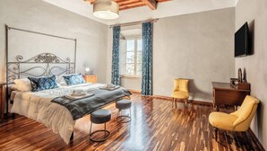 A bedroom with a wooden ceiling, a bed with a metal headboard, a nightstand, a desk, a chair, and a TV on the wall. - Spacious and wonderful apartment in the historic center with pets allowed (Lucca)