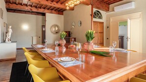 A dining area with a wooden table set for six, yellow chairs, and a rustic ceiling with exposed beams. - Spacious and wonderful apartment in the historic center with pets allowed (Lucca)