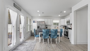 A modern kitchen with white cabinets, a stainless steel refrigerator, and a dining area with blue chairs.