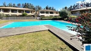 Una piscina con muelle de madera, rodeada por una valla blanca y abundante vegetación.