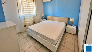 Un dormitorio con cama, mesitas de noche, lámpara, aire acondicionado y ventana con cortinas.