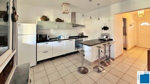 Una cocina moderna con armarios blancos, encimera negra y electrodomésticos de acero inoxidable. Hay tres taburetes de bar y una lámpara colgante.