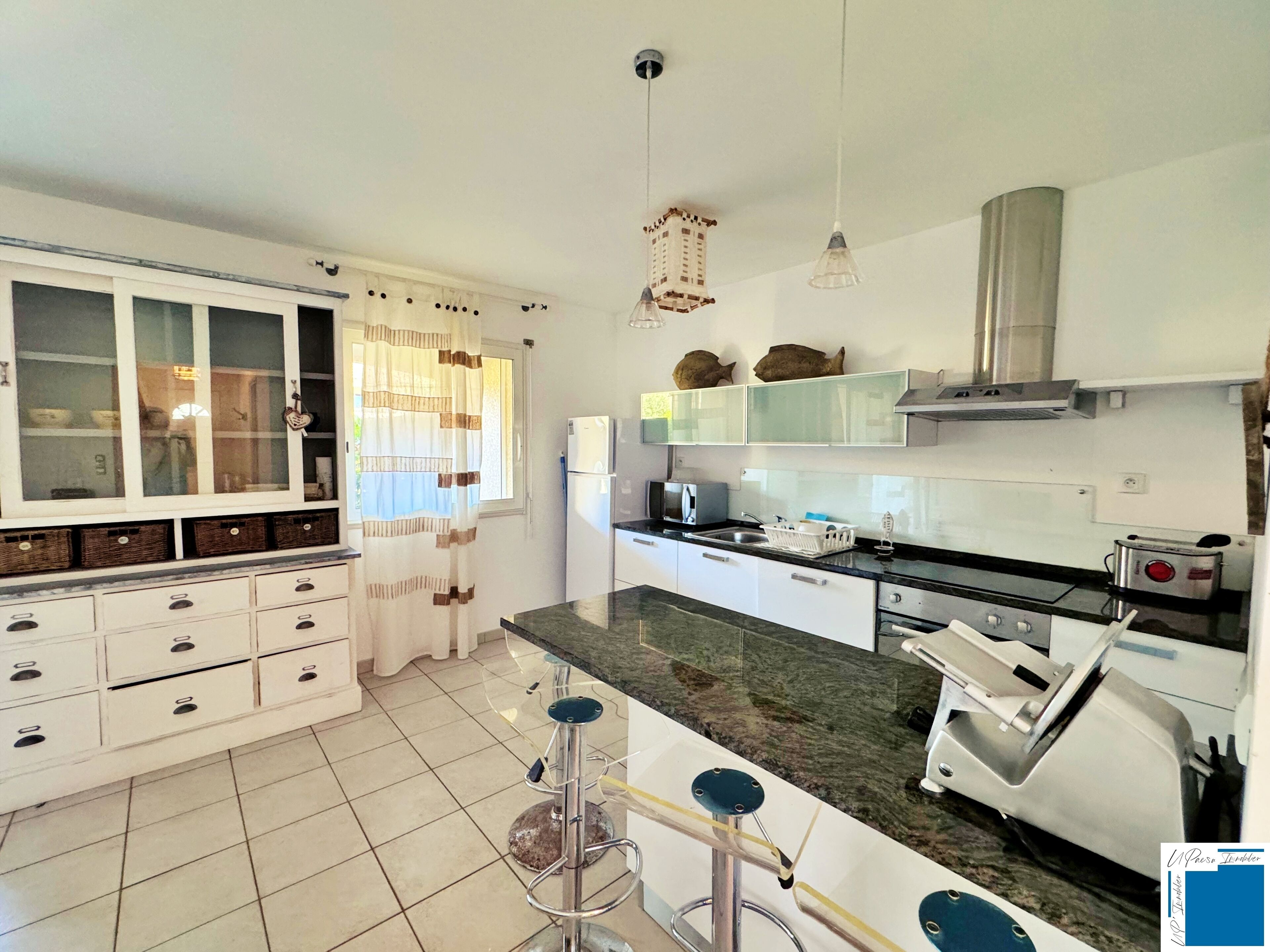 A kitchen with white cabinets, a marble countertop, a built-in stove, and a window with curtains.