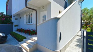 Un edificio moderno de dos pisos con techo plano, un pequeño porche con escalones y una puerta con contraventanas blancas.