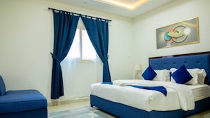 Une chambre d’hôtel avec un lit, un fauteuil bleu et un tableau accroché au mur.