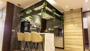 Un espace bar moderne avec un comptoir en marbre, trois tabourets et des plantes suspendues.