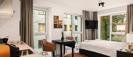 Una habitación de hotel moderna con cama, escritorio, silla, televisor y un ventanal con vistas a la ciudad.