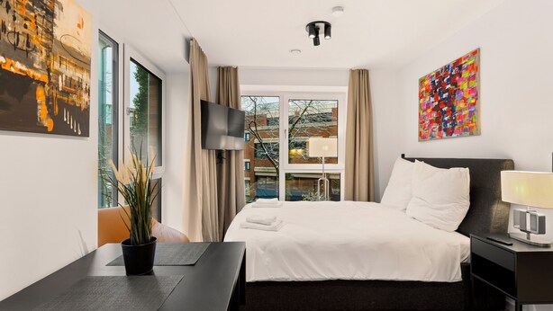 Habitación de hotel moderna con una cama grande, un escritorio, un televisor de pantalla plana y obras de arte en las paredes.