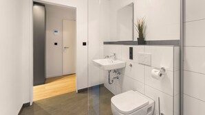 Un baño moderno con lavamanos, inodoro y zona de ducha blancos.