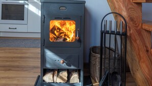 Een moderne keuken met een houtkachel, een houten trap en een mand vol houtblokken.