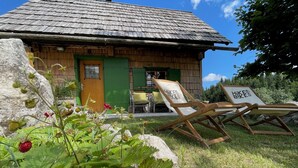 Een houten huis in rustieke stijl met rieten dak, een groene deur en een klein terras met twee houten loungesessels.