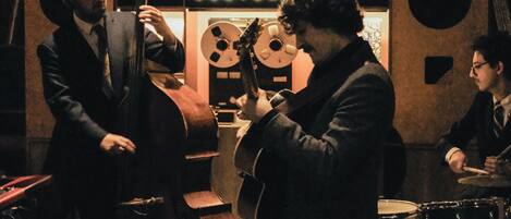 Una banda de jazz tocando en una sala con una estantería y un cartel que dice 'SUBTERF'.