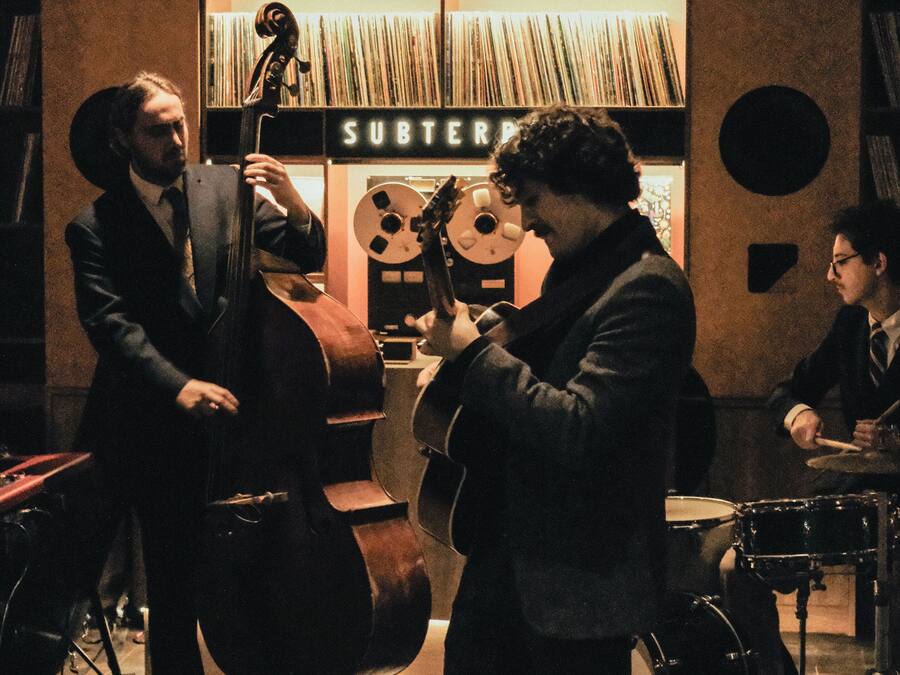A jazz band performing in a room with a bookshelf and a sign that reads 'SUBTERF'.