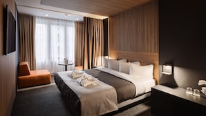 A modern hotel room with a large bed, a bedside table, a small table with a lamp, and a seating area with a chair. - SonoLux (Montréal)