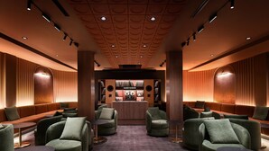 A modern lounge area with green upholstered seating, a central bar, and a patterned ceiling. - SonoLux (Montréal)