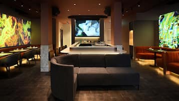 A modern bar area with a large screen, seating, and a bar counter.