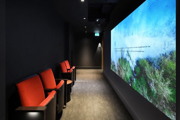 A cinema room with red chairs and a large screen displaying a nature scene.