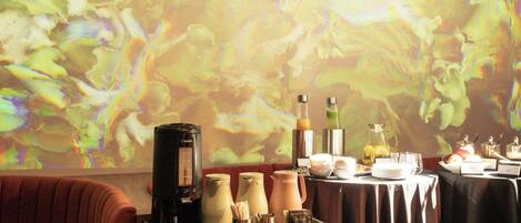 A dining area with a projection screen, a coffee machine, and a buffet table with various food items.