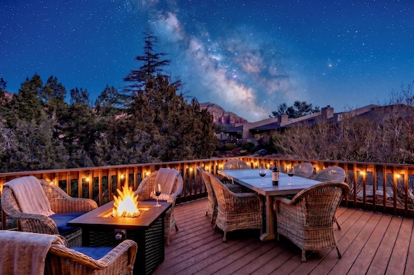 A deck with outdoor seating and a fire feature, surrounded by trees and a mountain backdrop under a starry sky.