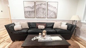 Ein Wohnzimmer mit einem dunklen Holztisch, einem schwarzen Ledersofa und einem Holzboden.
