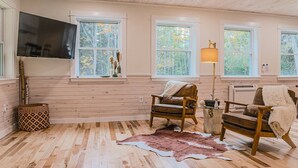 Ein gemütliches Blockhaus-Interieur mit Holzwänden, einem großen an der Wand befestigten Fernseher und zwei Ledersesseln mit Decken.
