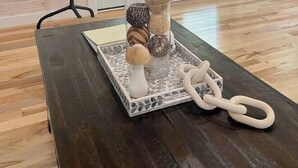 Ein Zimmer mit dunklem Holztisch, einem Kleiderständer und Blick auf eine grüne Außenanlage durch eine Glastür.