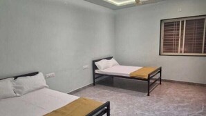 A room with two beds, a ceiling fan, recessed lighting, and a window with blinds. - Shri Swami Samarth Home Stay (Akalkot)